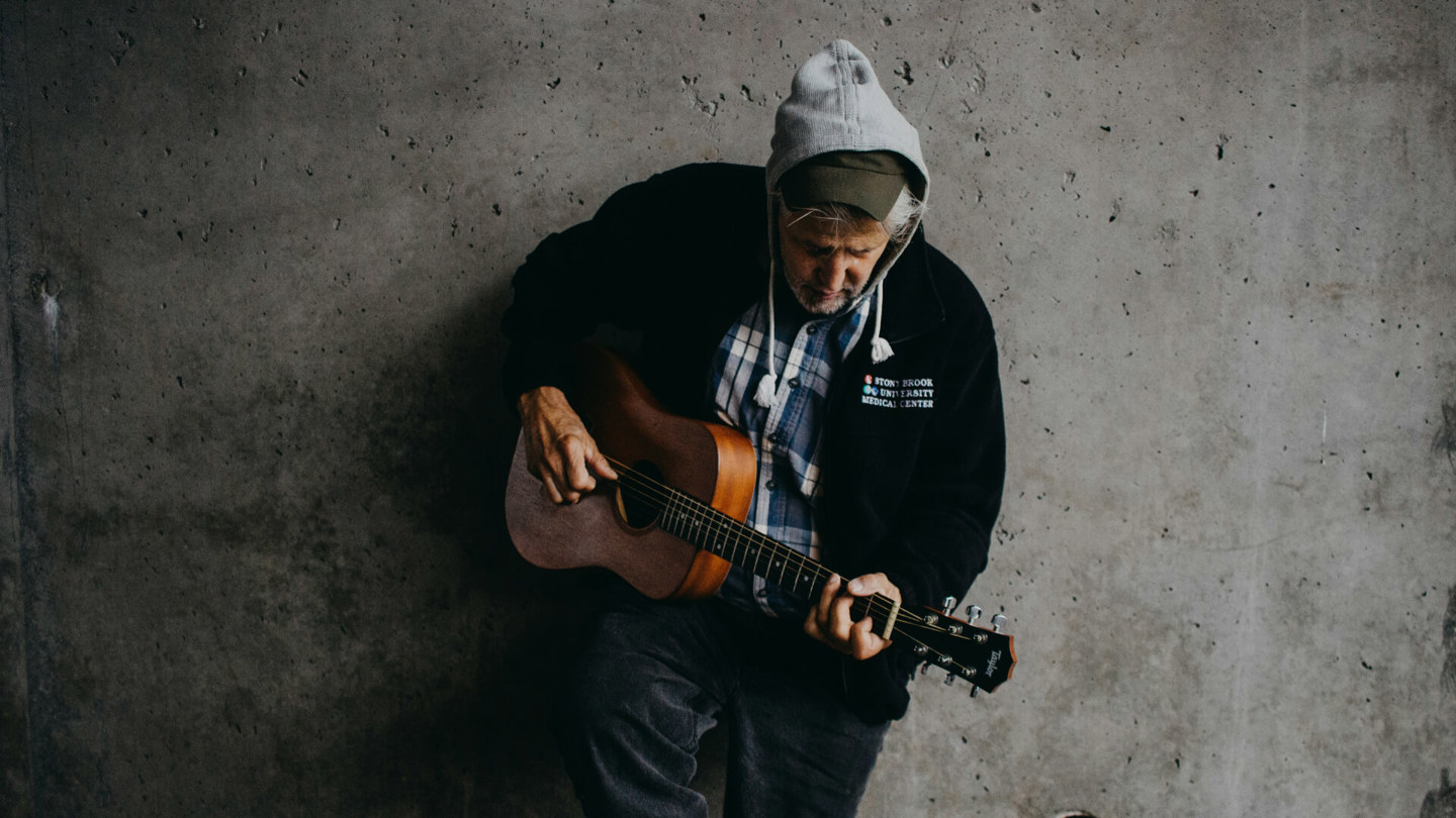 Ein Mann lehnt mit einer Gitarre an der Wand